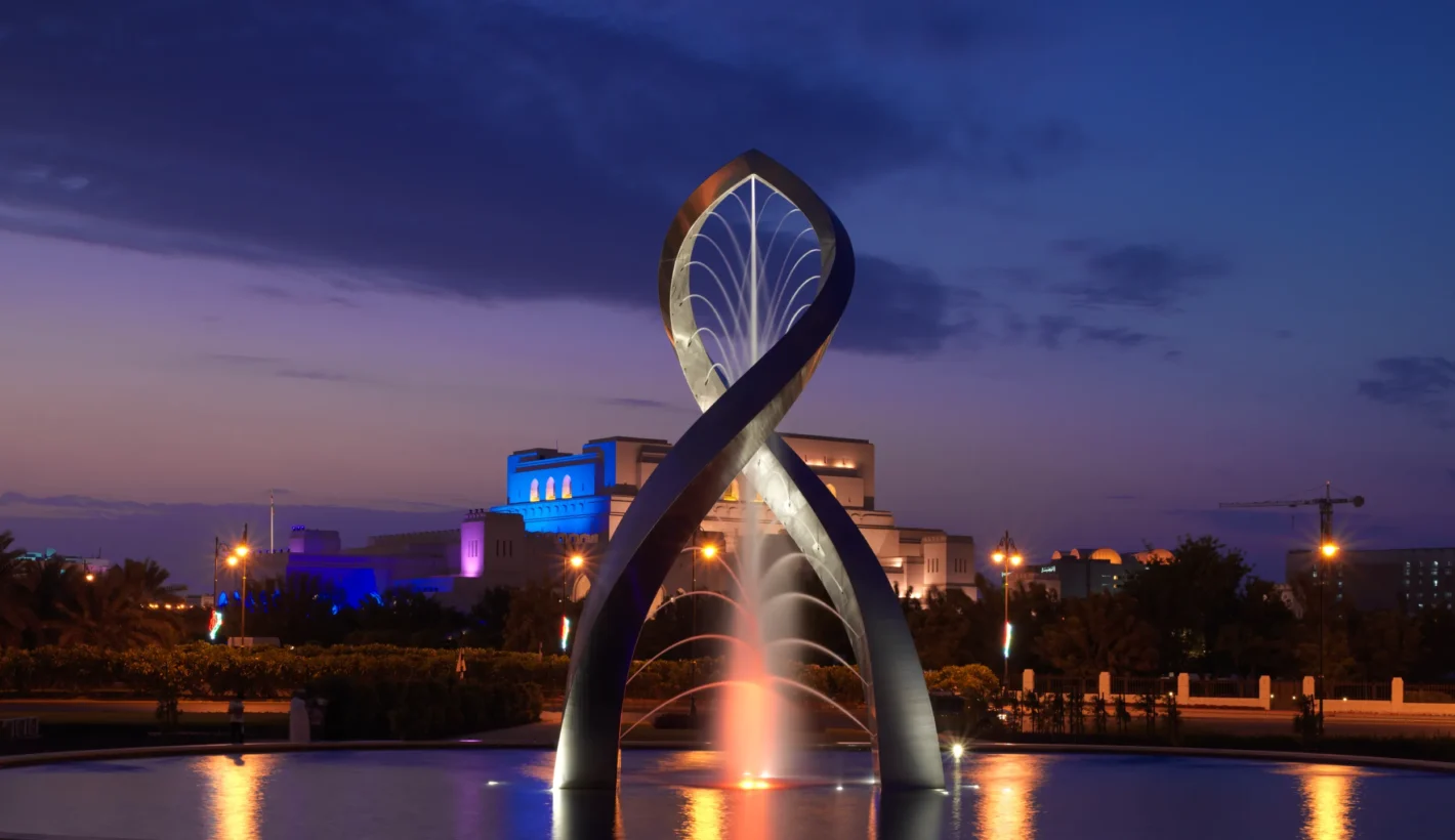 Arches of Oman sculpture in Muscat lit up at night time with purple sky background