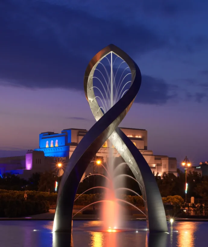 Arches of Oman sculpture in Muscat lit up at night time with purple sky background