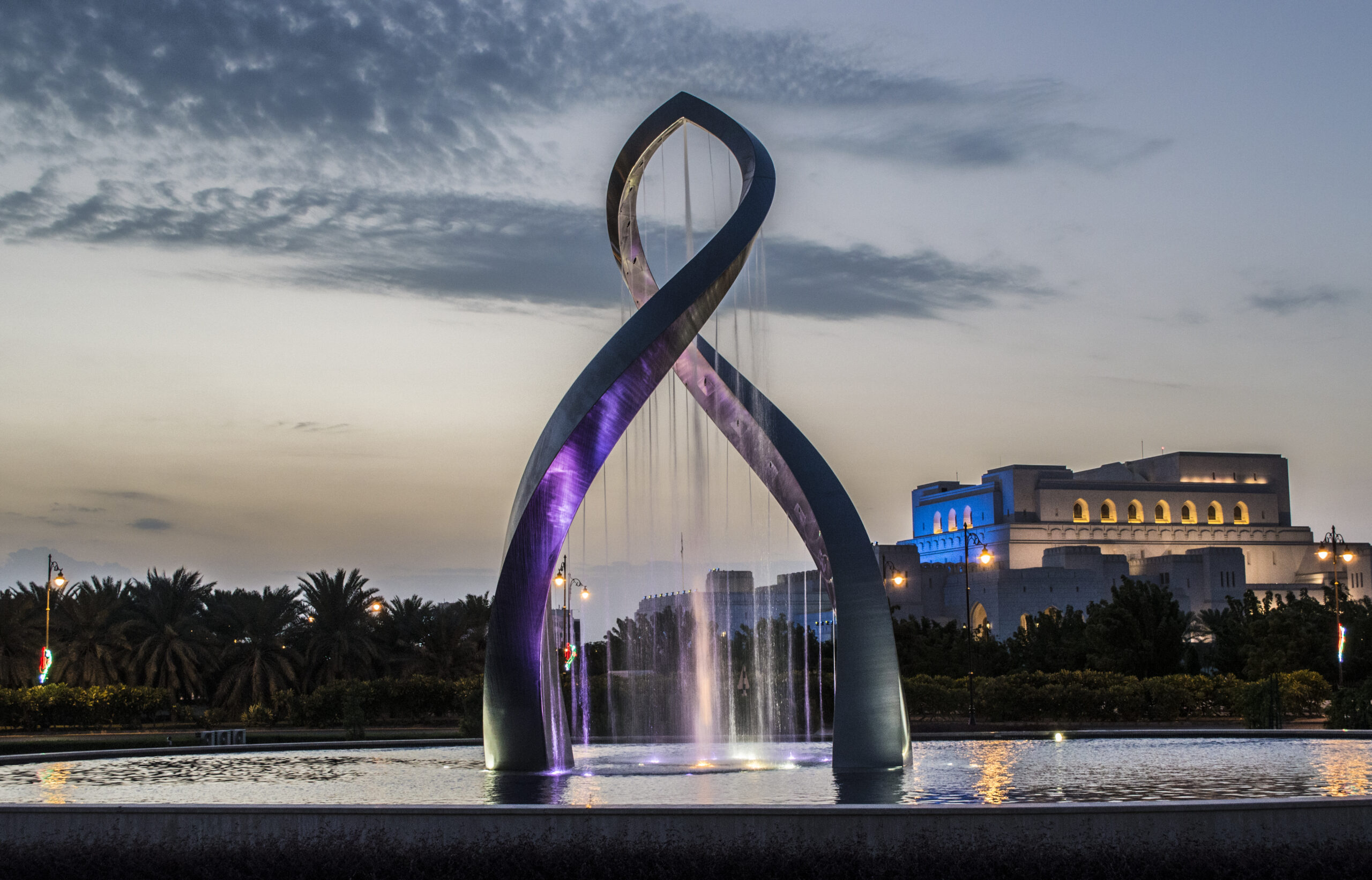 Dusk shot of the Arches of Oman in water in Muscat with building in the background